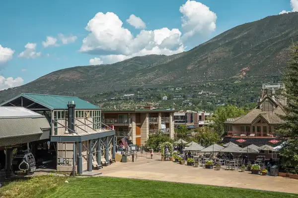 Outdoor scene of a town with mountains in the background and cable car station in the foreground, people walking and sitting outdoors