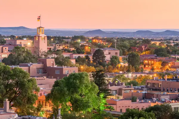 A cityscape of Santa Fe, New Mexico at sunset with buildings, trees and distant hills