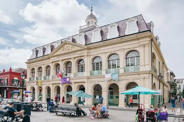 A historical building in New Orleans with people gathered outside, flags on display, and colorful decorations