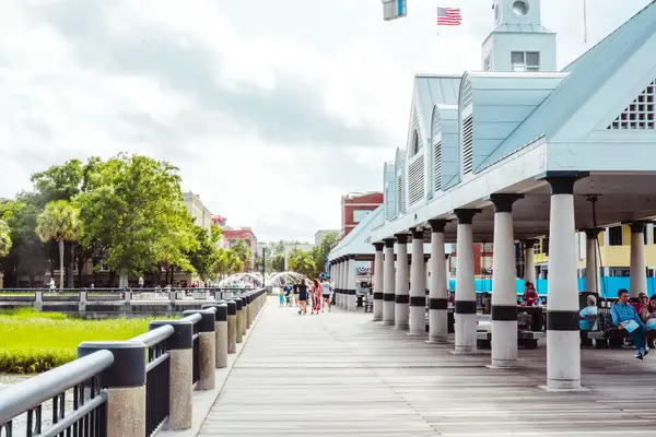 A boardwalk with people walking near a waterside pavilion under a partly cloudy sky